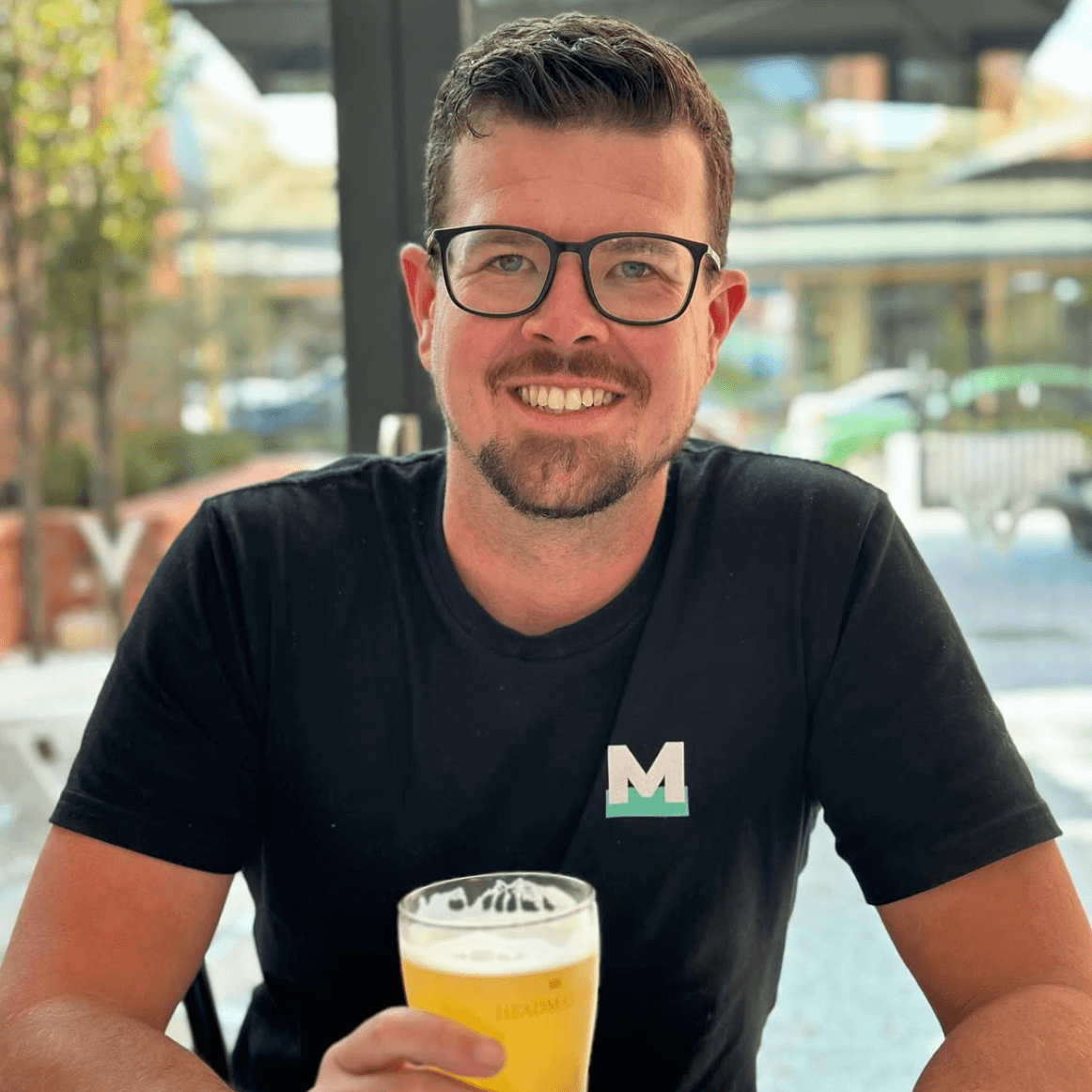 Man holding a beer in an outdoor setting with a blurred background